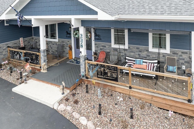 property entrance with a shingled roof, stone siding, and covered porch