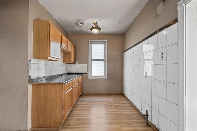 kitchen featuring light wood-type flooring, dark countertops, brown cabinets, decorative backsplash, and a sink