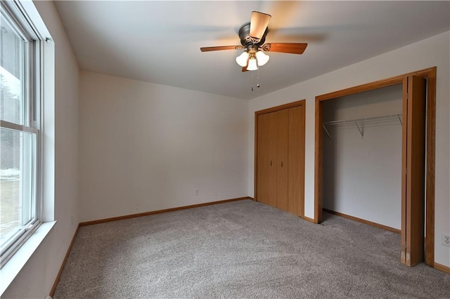 unfurnished bedroom featuring carpet, baseboards, two closets, and ceiling fan