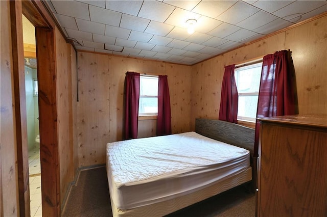 carpeted bedroom featuring wooden walls and multiple windows