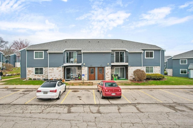 multi unit property with brick siding, uncovered parking, and a shingled roof