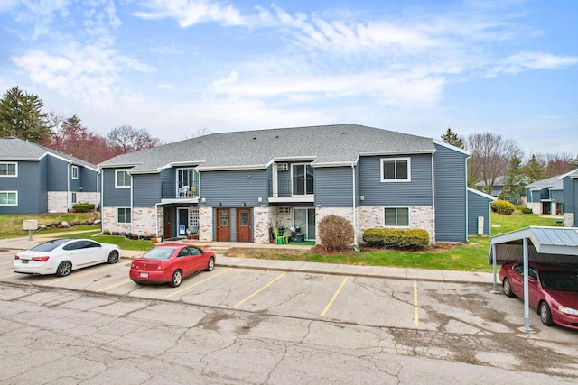 view of front facade with brick siding, a shingled roof, and uncovered parking