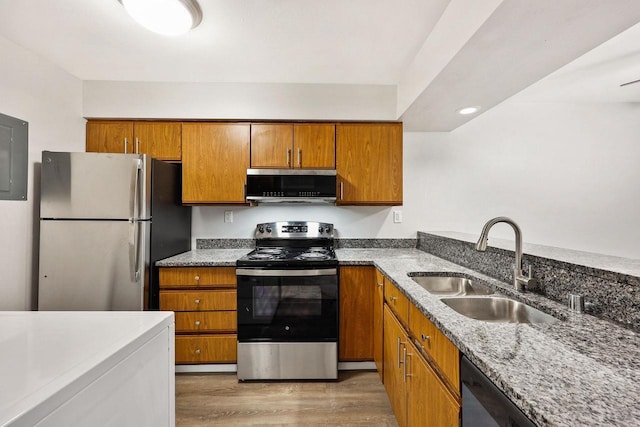 kitchen with a sink, light wood-type flooring, appliances with stainless steel finishes, brown cabinets, and light stone countertops