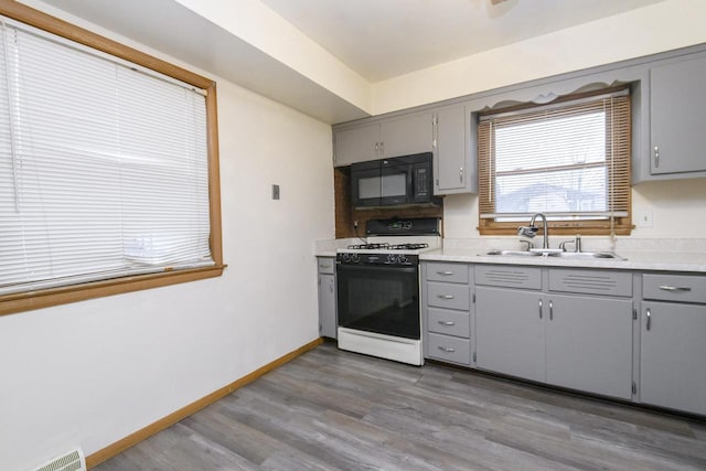 kitchen featuring a sink, black microwave, wood finished floors, gray cabinets, and gas range oven