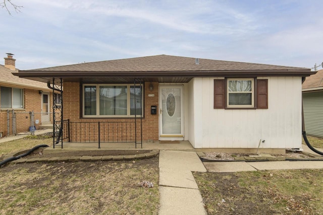 bungalow featuring brick siding, roof with shingles, a porch, and fence