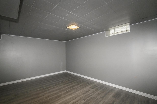 unfurnished room with a drop ceiling, baseboards, and dark wood-style floors