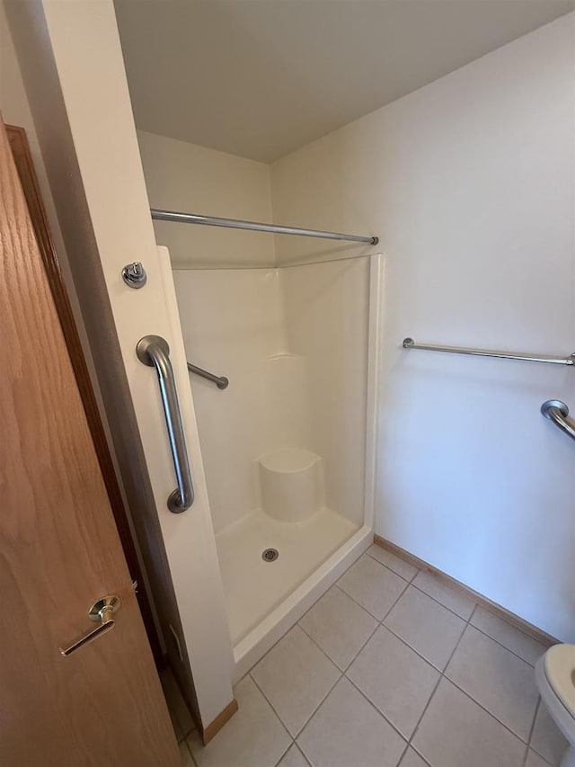 bathroom featuring toilet, a shower, tile patterned flooring, and baseboards