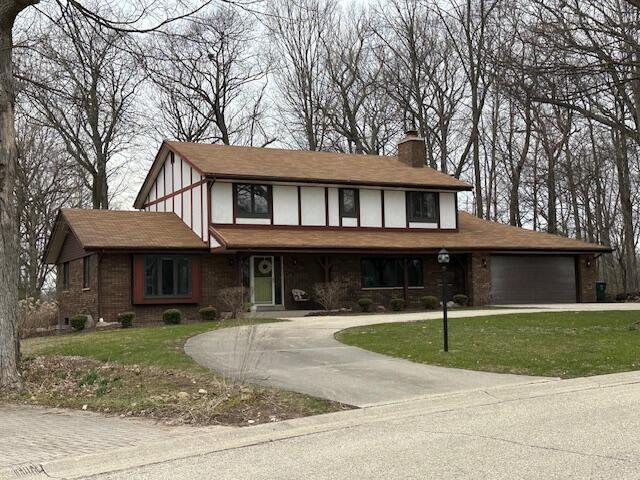 tudor house with a front lawn, a chimney, a garage, and curved driveway