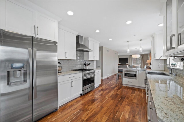 kitchen with dark wood-style floors, stainless steel appliances, wall chimney range hood, a sink, and white cabinetry