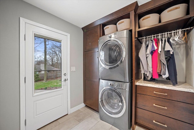 clothes washing area featuring baseboards, stacked washing maching and dryer, light tile patterned floors, and cabinet space