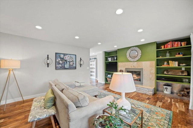 living room with wood finished floors, built in features, a tile fireplace, baseboards, and recessed lighting