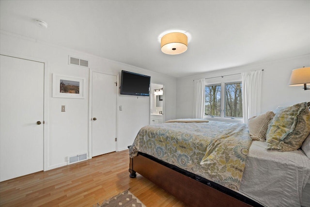 bedroom featuring light wood-style floors, visible vents, and connected bathroom