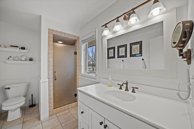 bathroom featuring tile patterned floors, a wainscoted wall, toilet, vanity, and a stall shower