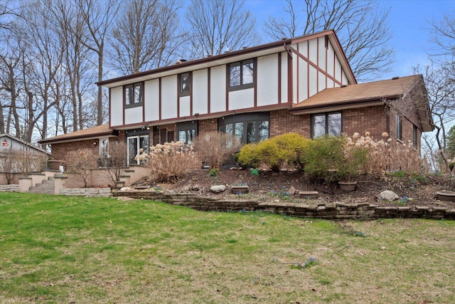 back of house featuring brick siding, a yard, and stucco siding