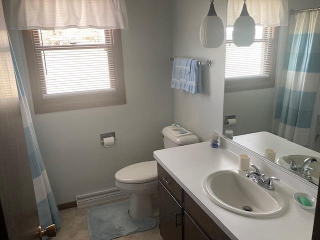 full bathroom with baseboards, curtained shower, toilet, baseboard heating, and vanity