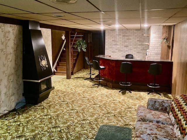 bar featuring a bar, a drop ceiling, and stairway