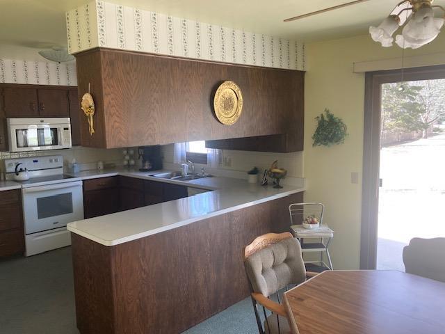 kitchen with white range with electric stovetop, a peninsula, light countertops, and a sink