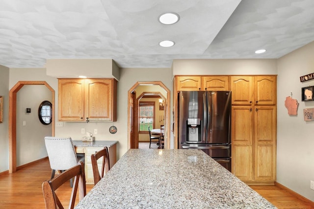 911 Chalfont Dr, Sun Prairie, WI 53590 - kitchen with light stone counters, stainless steel fridge with ice dispenser, arched walkways, light wood-style flooring, and baseboards