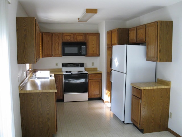 kitchen with black microwave, light countertops, freestanding refrigerator, brown cabinets, and range with electric cooktop