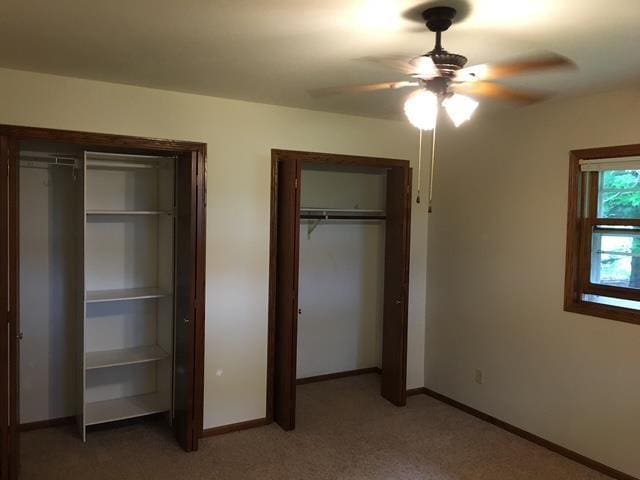 unfurnished bedroom with multiple closets, baseboards, ceiling fan, and light colored carpet