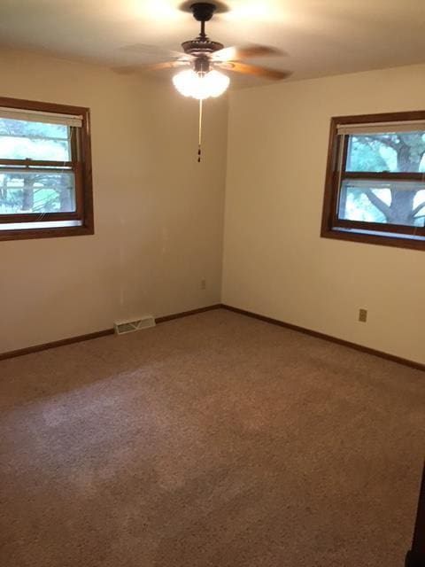 empty room with light carpet, visible vents, baseboards, and a ceiling fan