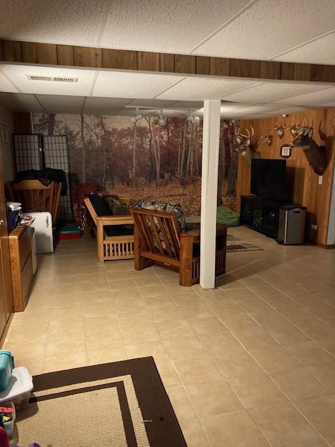 finished basement featuring wood walls, light tile patterned floors, visible vents, and a drop ceiling
