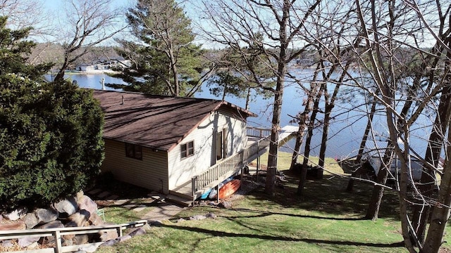 view of property exterior with stairway, a water view, a yard, and a shingled roof