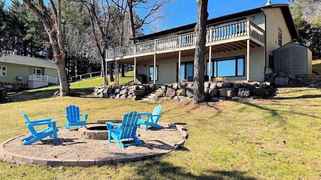 rear view of property with a storage unit, a wooden deck, a lawn, an outdoor structure, and an outdoor fire pit