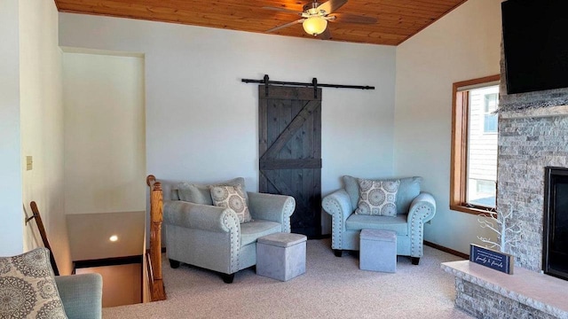 living area featuring a barn door, a ceiling fan, a stone fireplace, wood ceiling, and carpet flooring