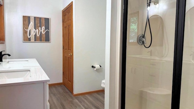 full bathroom with a shower stall, wood finished floors, double vanity, toilet, and a sink