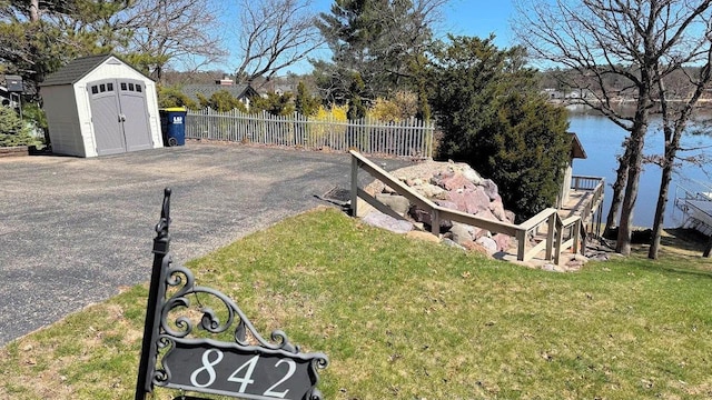 view of yard featuring a storage unit, an outbuilding, a water view, and fence
