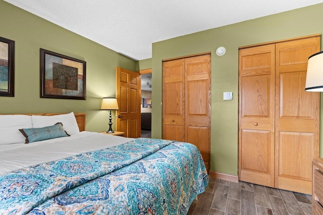 bedroom with dark wood-type flooring, baseboards, and two closets