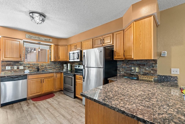 kitchen with a sink, light wood-style floors, a textured ceiling, stainless steel appliances, and decorative backsplash