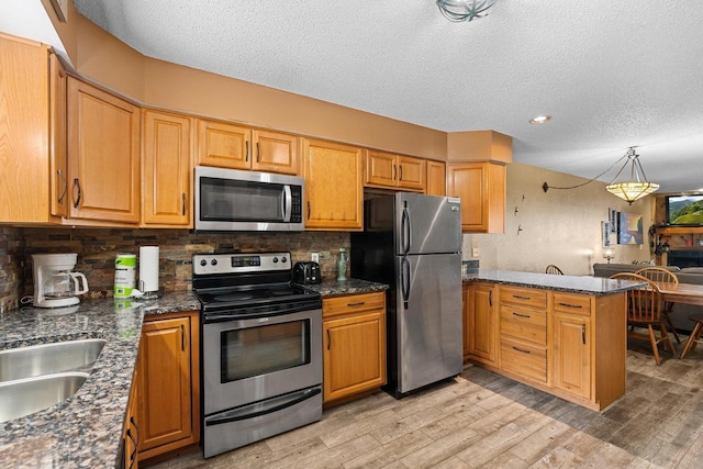 kitchen featuring stainless steel appliances, a peninsula, light wood-style floors, and a textured ceiling