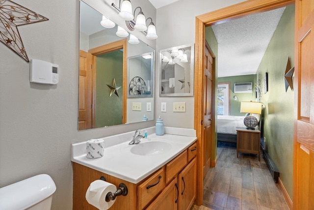 bathroom with toilet, hardwood / wood-style flooring, connected bathroom, vanity, and a wall unit AC
