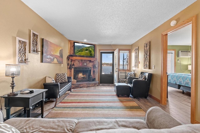 living area with a fireplace, a textured ceiling, a wall unit AC, wood finished floors, and baseboards