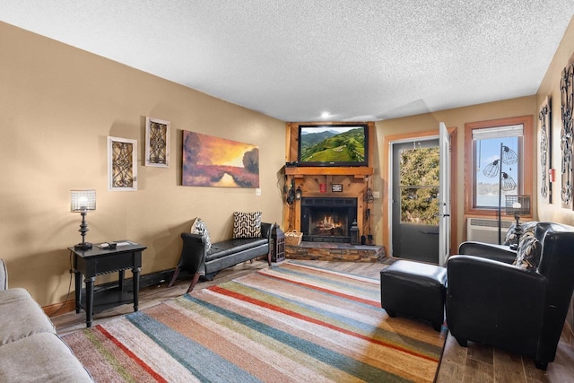 living room featuring a stone fireplace, a wall mounted air conditioner, wood finished floors, and a textured ceiling