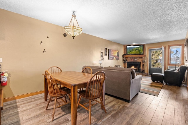 dining space featuring baseboards, light wood-type flooring, a lit fireplace, and a textured ceiling