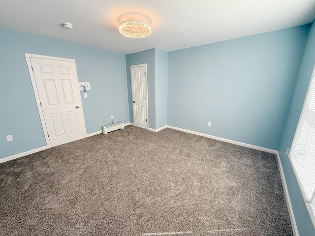 carpeted spare room featuring a baseboard heating unit and baseboards