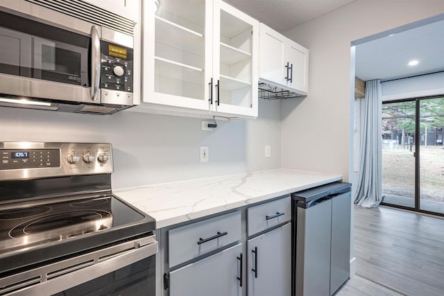 kitchen with glass insert cabinets, white cabinetry, light wood-style flooring, light stone countertops, and stainless steel appliances