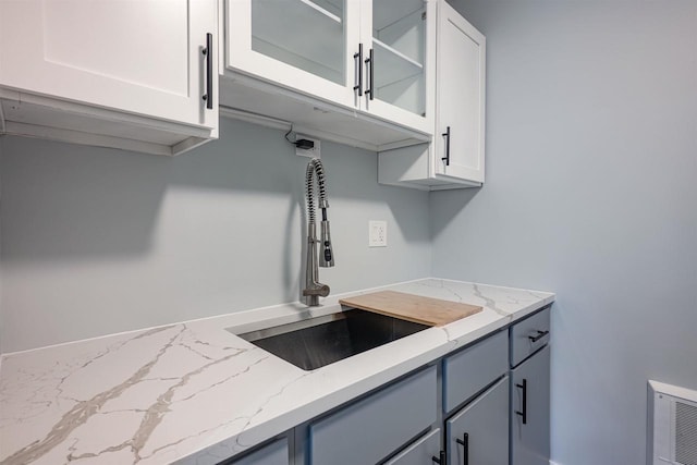 kitchen featuring a sink, glass insert cabinets, white cabinets, and light stone countertops