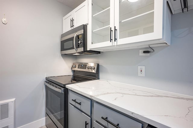kitchen featuring glass insert cabinets, white cabinets, appliances with stainless steel finishes, light stone counters, and baseboards