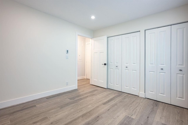 unfurnished bedroom featuring light wood-style flooring, multiple closets, recessed lighting, and baseboards