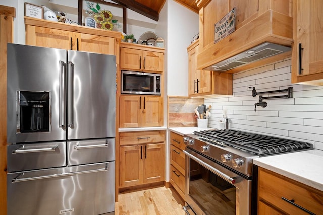 1979 9th Ave, Friendship, WI 53934 - kitchen featuring light wood finished floors, decorative backsplash, custom exhaust hood, light countertops, and appliances with stainless steel finishes