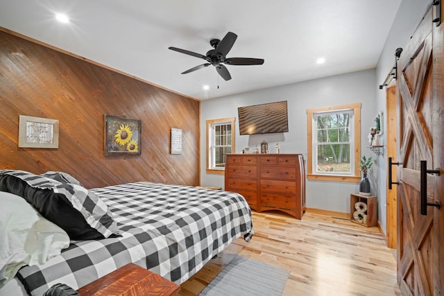 1979 9th Ave, Friendship, WI 53934 - bedroom featuring recessed lighting, a barn door, ceiling fan, wooden walls, and light wood-style flooring