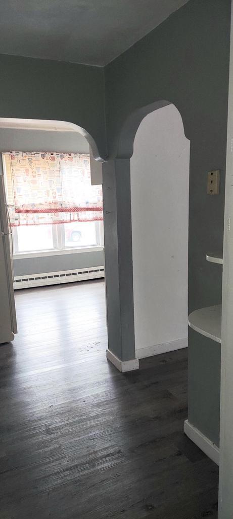 140 E Ave, Iron Ridge, WI 53035 - empty room featuring arched walkways, dark wood-type flooring, a baseboard radiator, and baseboards