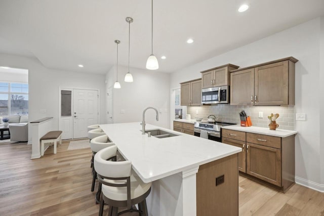 kitchen with a sink, light wood-type flooring, a center island with sink, decorative backsplash, and stainless steel appliances
