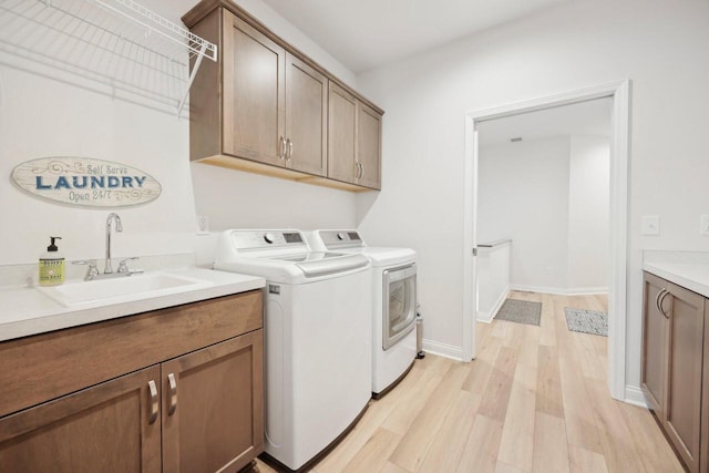 washroom featuring light wood-style floors, washing machine and dryer, a sink, and cabinet space