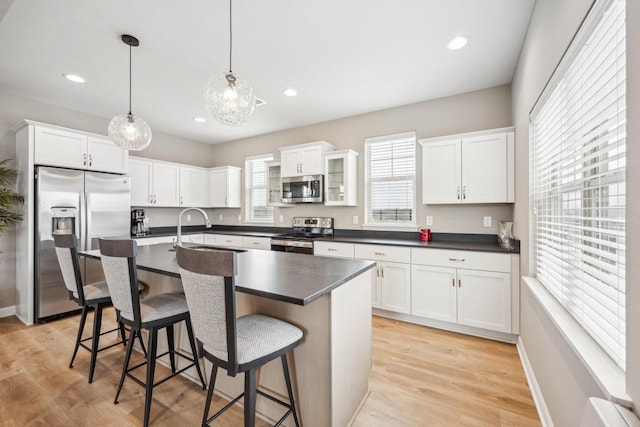 kitchen with a kitchen breakfast bar, white cabinetry, dark countertops, a sink, and stainless steel appliances