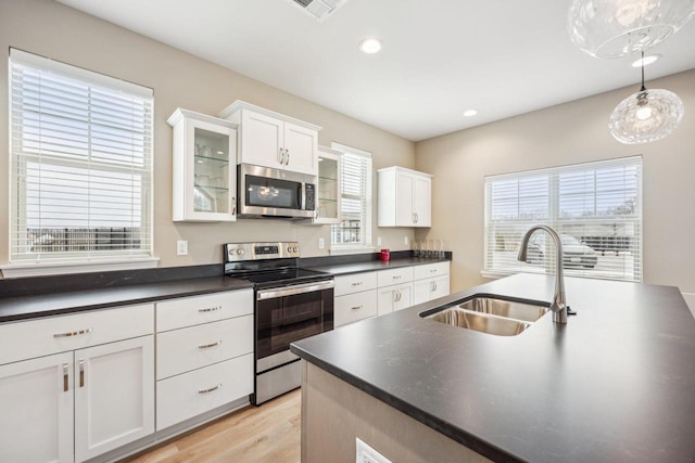 kitchen with white cabinetry, dark countertops, a sink, stainless steel appliances, and light wood finished floors